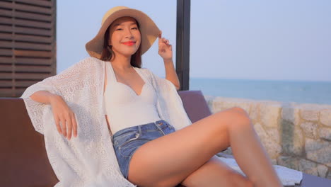 Slow-motion-on-Asian-woman-sitting-on-beach-chair-next-to-the-sea-posing-and-smiling-in-camera