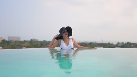A-woman-relaxing-at-the-edge-of-a-resort-infinity-pool-adjusts-her-sun-hat
