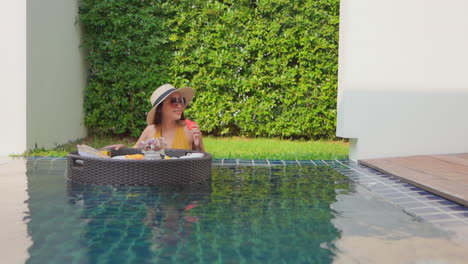 A-woman-in-a-swimming-pool-looks-over-the-floating-service-tray-choosing-a-piece-of-fruit-to-eat