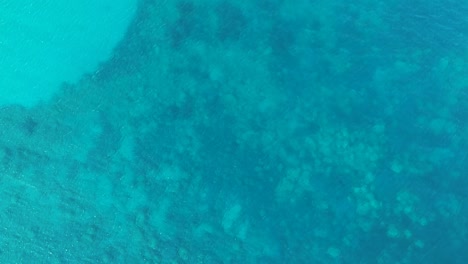 Clear-turquoise-blue-water-with-coral-reefs-below-on-the-island-of-Zakynthos-Greece,-Aerial-drone-lift-view-from-above