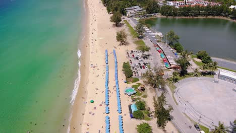 Aerial-tilt-of-umbrellas-aligned-on-a-tropical-beach-in-Phuket,-Thailand