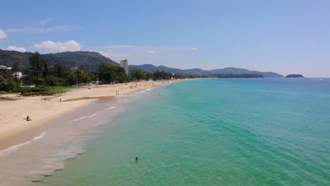 Low-aerial-drone-shot-along-beautiful-sandy-coastline-of-Phuket,-summer,-people