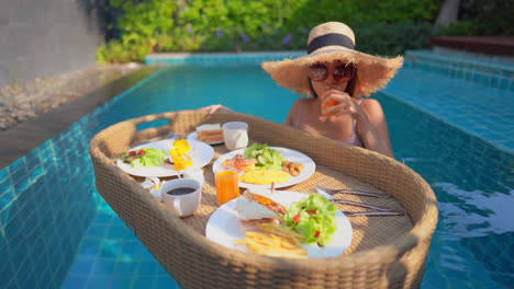 A-young-woman-tourist-has-her-own-personal-breakfast-on-a-floating-table-in-a-private-swimming-pool