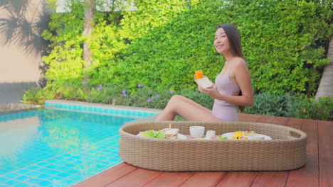 Joyous-happy-asian-lady-having-breakfast-next-to-a-pool,-medium-shot