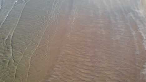 Calm-clear-ocean-waves-gently-cover-sand-beach-in-soft-daylight