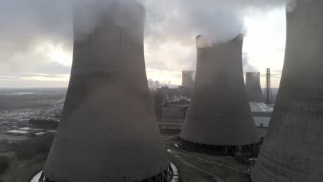 Aerial-dolly-right-view-of-UK-power-station-cooling-towers-smoke-steam-emissions,-sunrise-reveal-behind-chimney