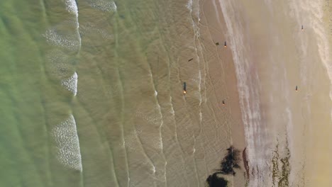 High-aerial-top-down-view-of-waves-breaking-on-beach,-people-in-water,-fly-over-jetty-and-beach