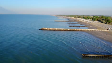 Drone-seascape-along-beach,-jetty,-long-range-view,-people,-over-water