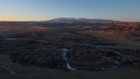 Aerial-view-flying-away-from-mountains-and-a-river-at-sunset-in-Montana