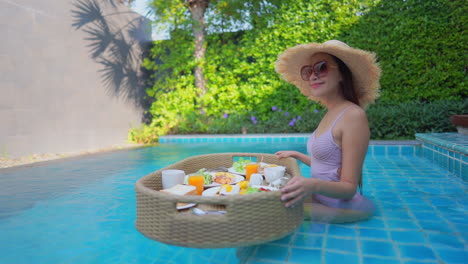 Beautiful-mixed-race-happy-Woman-sitting-on-swimming-pool-holding-breakfast-floating-tray