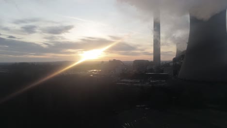 Aerial-view-of-power-station-cooling-towers-burning-smoke-emissions-with-atmospheric-glowing-sunrise-low-dolly-right
