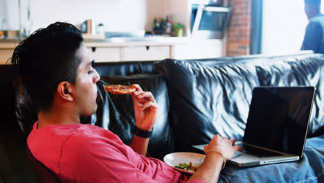 Mann-Isst-Essen,-Während-Er-Im-Wohnzimmer-Einen-Laptop-Benutzt