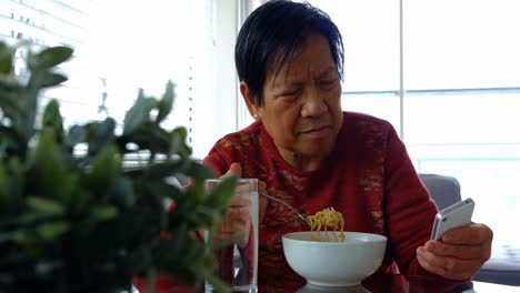 Senior-woman-using-mobile-phone-while-having-food