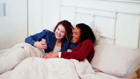 Lesbian-couple-using-mobile-phone-on-bed