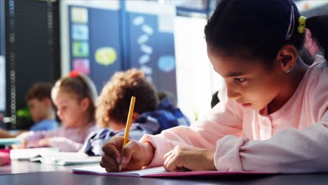 Attentive-schoolgirl-doing-her-homework-in-classroom