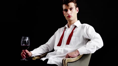 Androgynous-man-holding-wine-glass-against-black-background