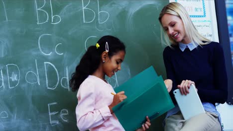 Teacher-helping-schoolgirl-with-her-homework-in-classroom