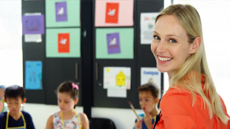 Portrait-of-smiling-teacher-assisting-schoolkid-in-drawing-class