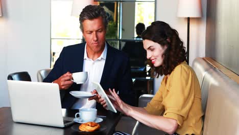 Businessman-and-colleague-discussing-over-digital-tablet-while-having-coffee