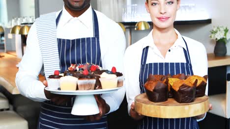 Portrait-of-smiling-waiter-and-waitress-presenting-desserts-at-counter