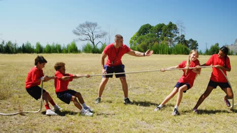 Trainer-assisting-kids-in-tug-of-war-during-obstacle-course-training
