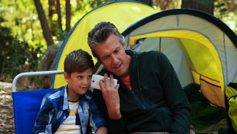 Father-and-son-using-mobile-phone-outside-tent