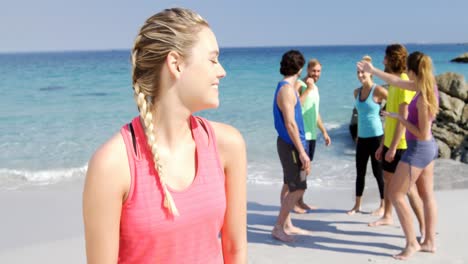 Fit-woman-smiling-at-camera-while-friends-interacting-behind-her-at-beach