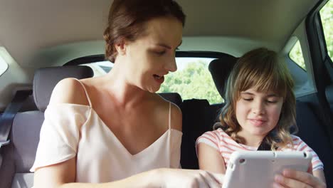 Madre-E-Hija-Usando-Una-Tableta-Digital-En-El-Asiento-Trasero-Del-Auto