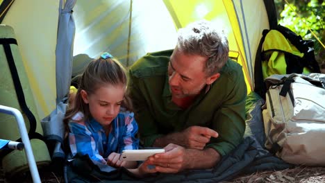 Father-and-daughter-using-mobile-phone-outside-tent