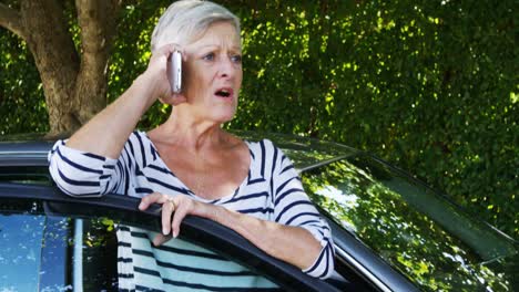 Senior-woman-talking-on-mobile-phone-near-car