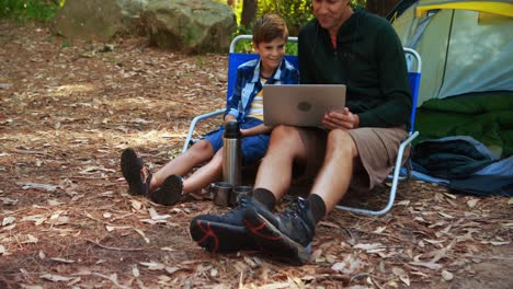 Father-and-son-using-laptop-outside-tent