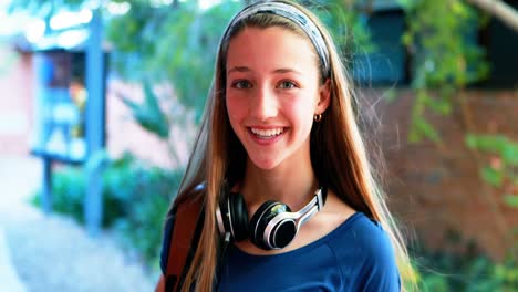 Smiling-schoolgirl-standing-with-schoolbag-in-campus