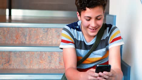 Schoolboy-sitting-on-staircase-and-using-mobile-phone