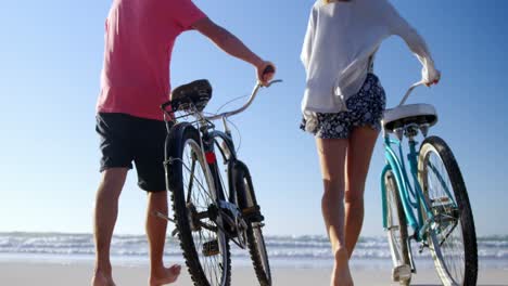Paar-Geht-An-Einem-Sonnigen-Tag-Mit-Fahrrädern-Am-Strand-Spazieren