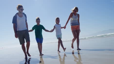 Family-holding-hands-while-walking-on-shore-at-beach