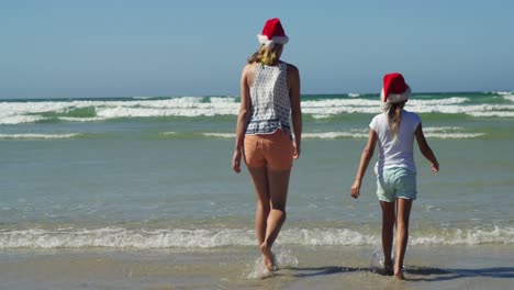 Mother-and-daughter-walking-on-shore-at-beach-on-a-sunny-day