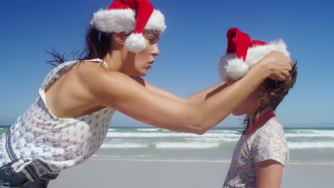 Mutter-Setzt-Mädchen-Am-Strand-Weihnachtsmütze-Auf-Den-Kopf