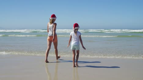 Mother-and-daughter-walking-on-shore-at-beach-on-a-sunny-day