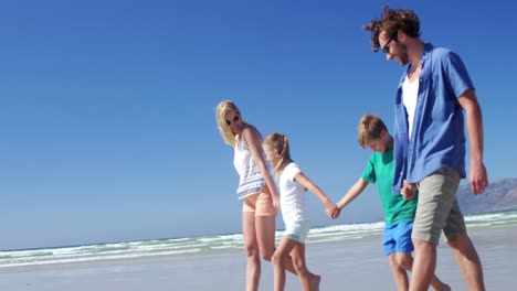 Family-holding-hands-while-walking-on-shore-at-beach