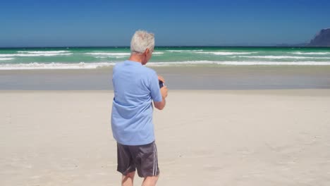 Senior-man-taking-photo-from-mobile-phone-at-beach