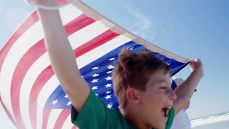 Geschwister-Halten-Die-Amerikanische-Flagge-In-Der-Hand,-Während-Sie-Am-Ufer-Am-Strand-Laufen