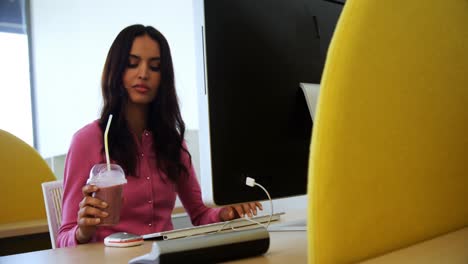 Executive-working-on-personal-computer-while-having-milkshake