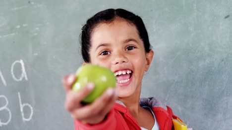 Smiling-schoolgirl-showing-apple-in-classroom