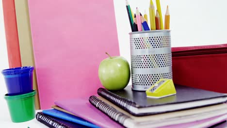 Colored-pencils-in-pen-holder-with-pile-of-books,-apple-and-stationery