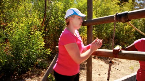 Trainer-assisting-woman-while-exercising-during-obstacle-course