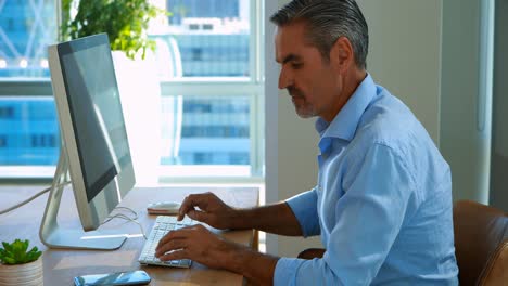 Male-executive-talking-on-mobile-phone-while-working-over-computer-at-his-desk