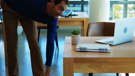 Male-executive-doing-stretching-exercise-while-working-at-his-desk