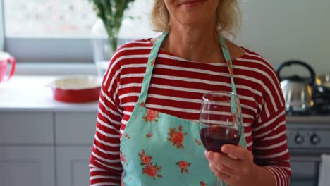 Portrait-of-smiling-woman-showing-a-glass-of-red-wine-in-kitchen