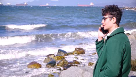 Man-talking-on-mobile-phone-at-beach-on-a-sunny-day-4k
