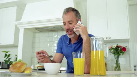 Man-talking-on-mobile-phone-while-having-breakfast-on-dining-table